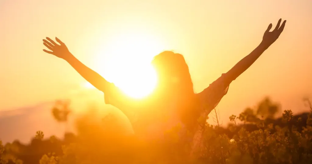 Woman with arms raised in joy, with a bright sun in the background