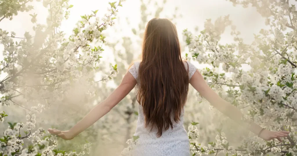 Woman with long brown hair with arms outstretched at a 45 degree angle, with spring flowers in the background