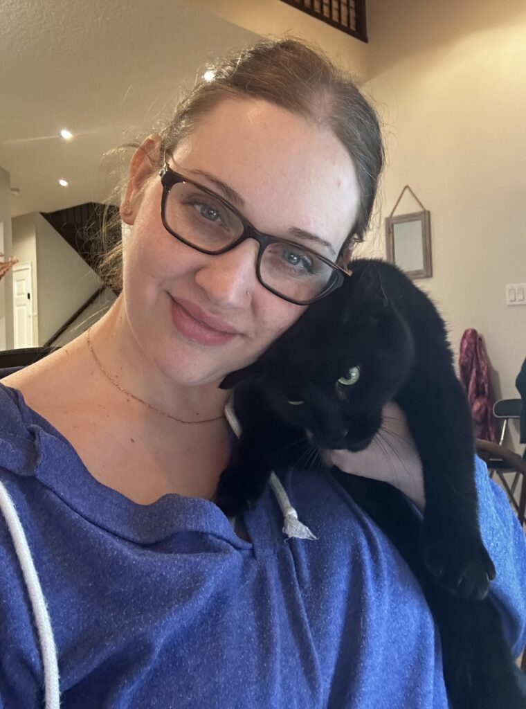 Woman in blue shirt holding a black cat with green eyes
